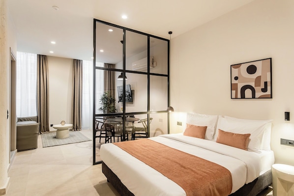 Une chambre d’hôtel moderne dotée d’un grand lit, d’un coin repas et d’une porte-fenêtre coulissante donnant sur un balcon.