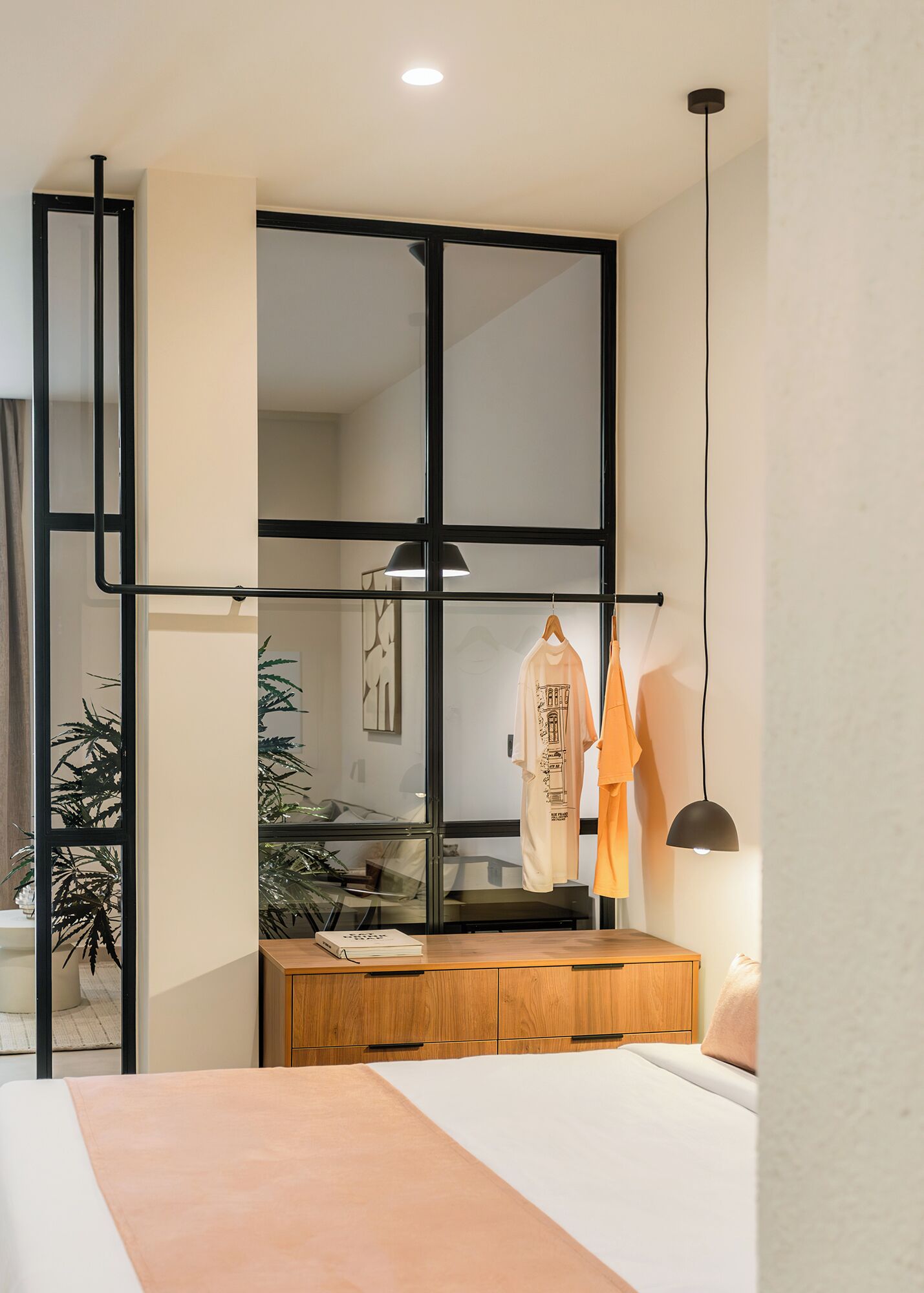 A bedroom with a bed, a wooden dresser, a mirror, and a hanging light fixture.
