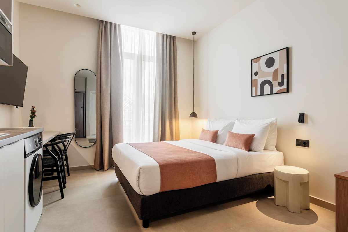 A modern hotel room with a bed, bedside table, and a large window with curtains.
