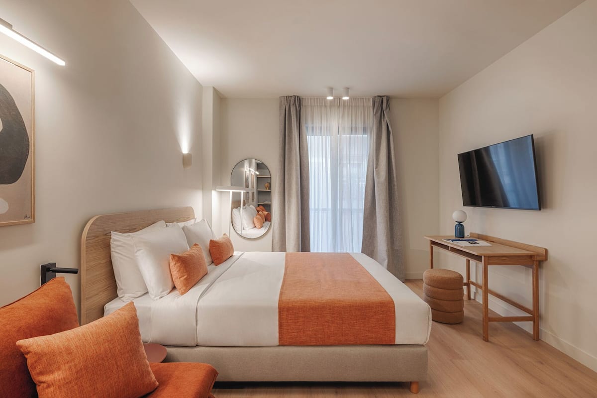 A hotel room with a bed, a desk, a television, and a large window with curtains.