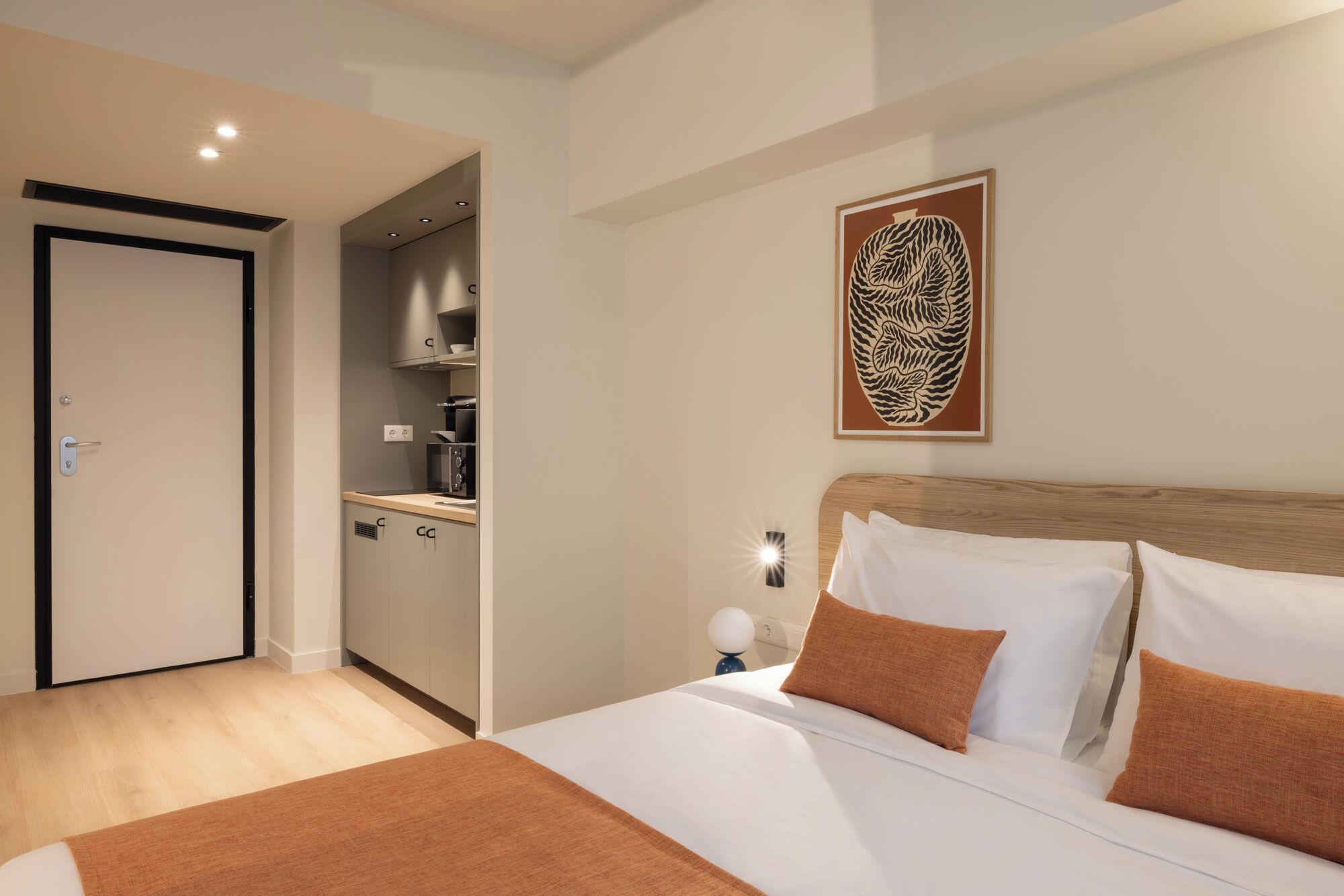 Ein Hotelzimmer mit Bett, Nachttisch, einem Wandbild und einer Küchenzeile.