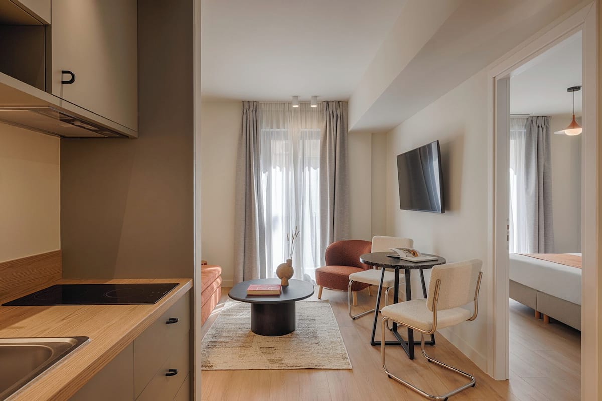 A modern living room with a sofa, chairs, a coffee table, a flat-screen TV, and a kitchen area with a stove.