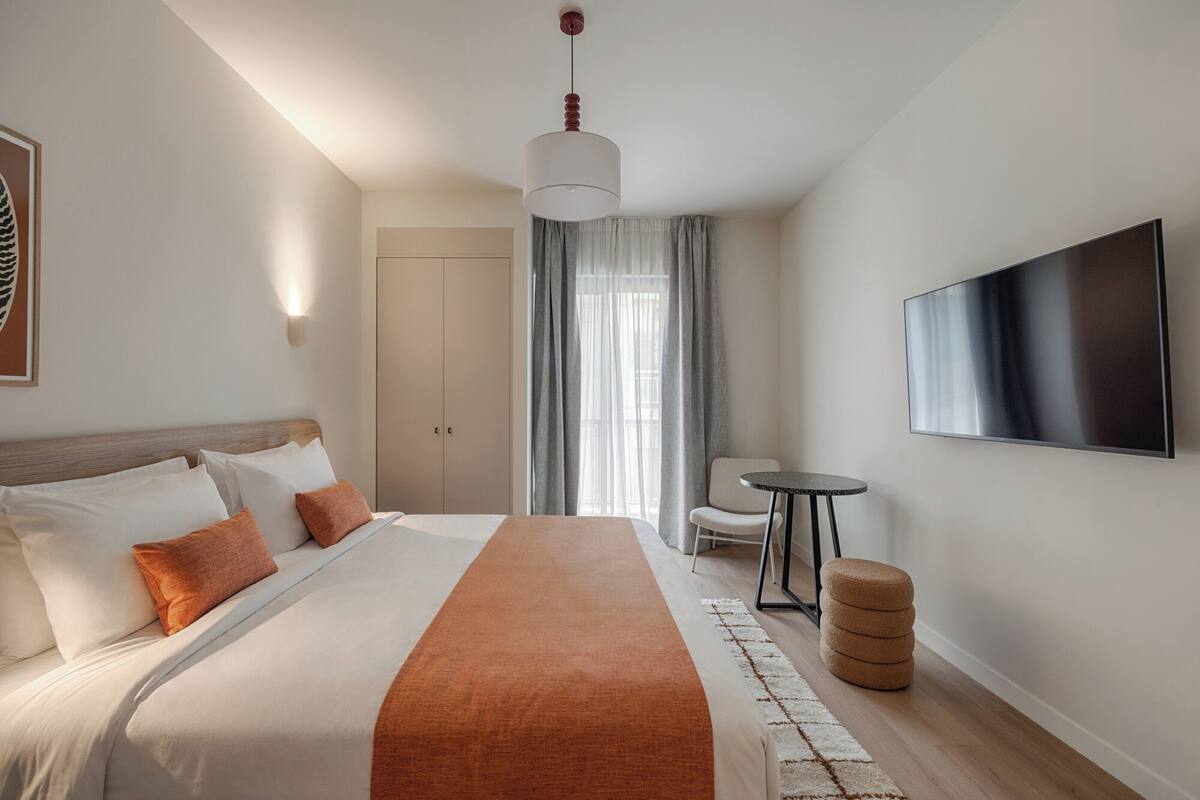 A hotel room with a large bed, a television, a chair, and a small table.