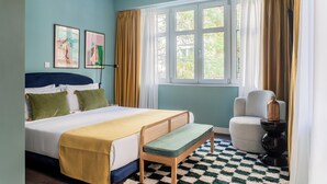 A bedroom with a bed, a bench, a chair, a table, and a window with curtains. - Didot by Zoia Living (Athina)