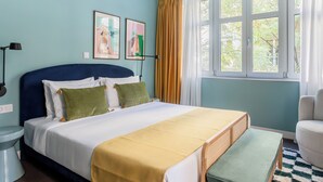 A bedroom with a bed, a bedside table, a lamp, a window with curtains, and a chair. - Didot by Zoia Living (Athina)