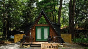 A small cabin with a green door, a sign reading 'The Shed,' and a wooden fence. - Romantic AFrame| Firepit| Grill | Projector | Pets (Pocono Pines)