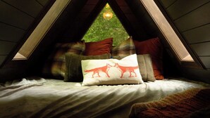 A cozy attic bedroom with a sloped ceiling, a bed with pillows, and a window with a view of greenery. - Romantic AFrame| Firepit| Grill | Projector | Pets (Pocono Pines)