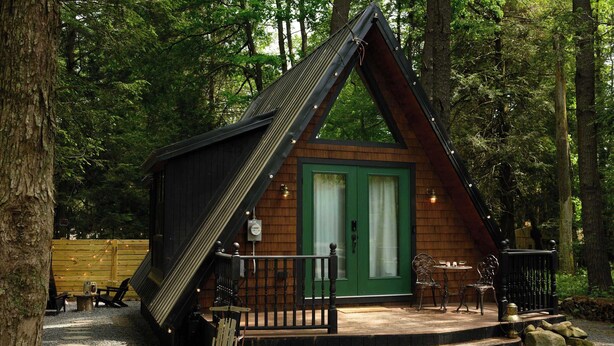 A small cabin with a green door, a wooden deck, and a staircase leading to the entrance. - Romantic AFrame| Firepit| Grill | Projector | Pets (Pocono Pines)
