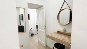 Un corridoio con un bancone in legno e uno sgabello, uno specchio e una porta che dà su un'altra stanza.