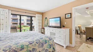A hotel room with a bed, a TV, a dresser, and a balcony with a view of the sea. - ✨Ocean and Pool Views | 1st Floor with Private Patio | Castle Reef 109✨ (New Smyrna Beach)