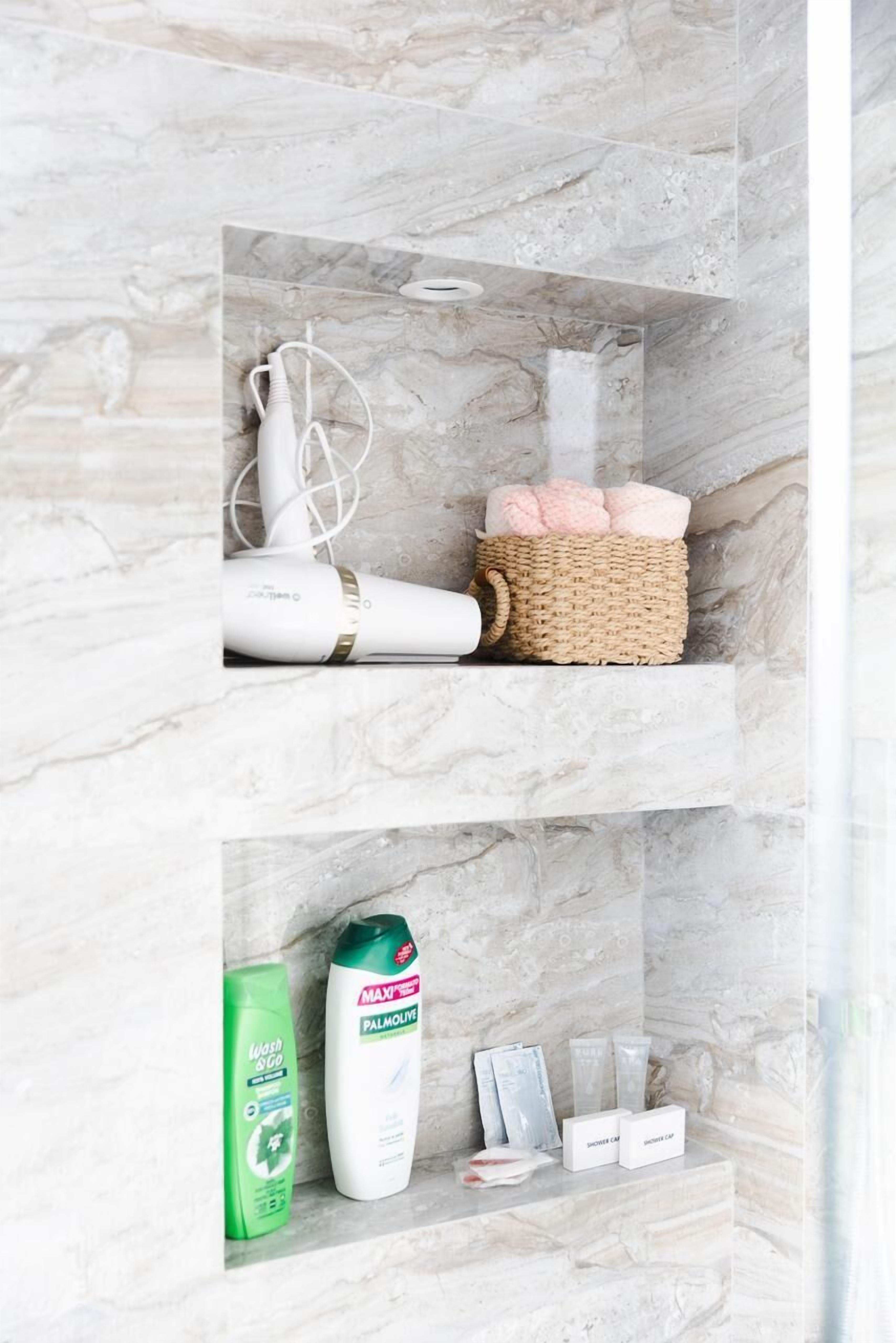 A bathroom with marble walls, a hairdryer, a basket with bath towels, and toiletries.