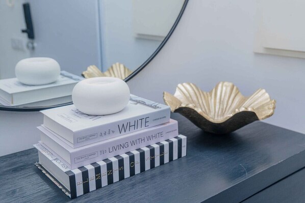 Une pile de livres intitulés « WHITE » et « LIVING WITH WHITE » est posée sur une surface sombre, avec un coquillage décoratif et un objet rond à proximité.