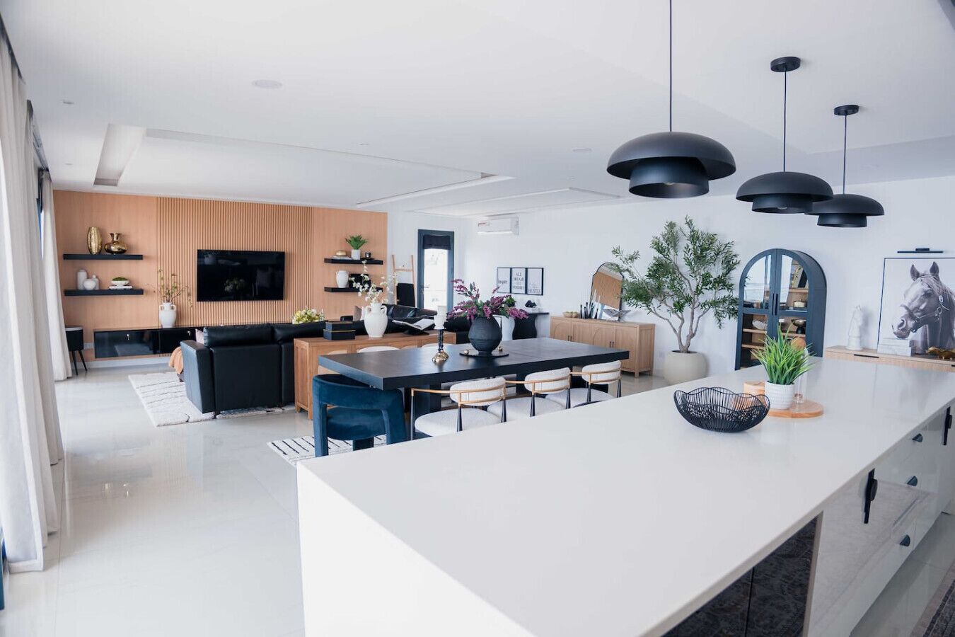 A modern kitchen with a central island, black pendant lighting, and a dining area with chairs.
