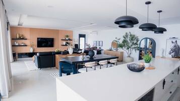A modern kitchen with a central island, black pendant lighting, and a dining area with chairs.