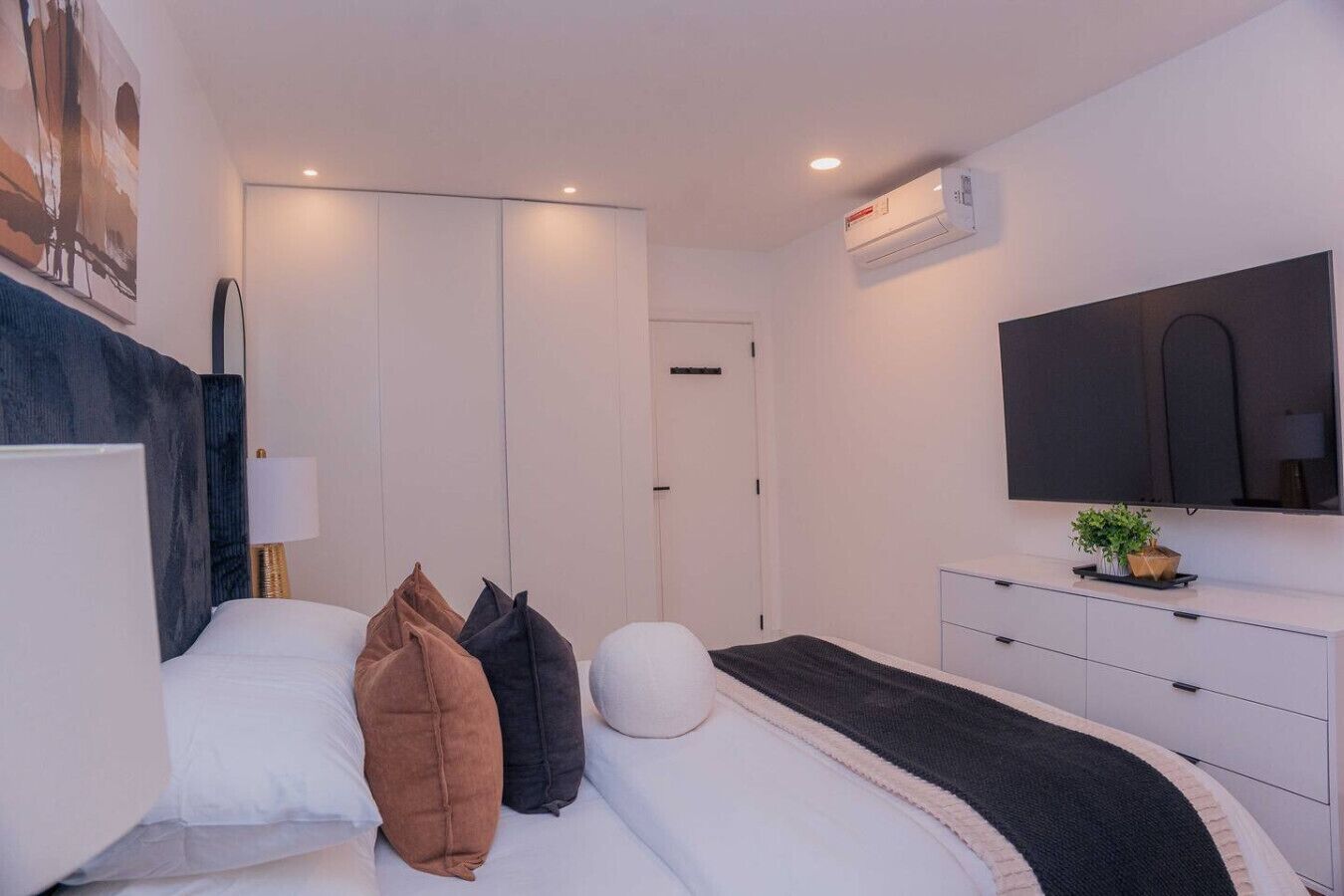 Une chambre à coucher moderne avec un lit, des oreillers, une lampe de chevet, un téléviseur et une petite plante.