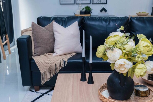 A modern living room with a dark blue leather sofa, a beige throw blanket, and a vase with flowers. - 5-Star Luxury OCEAN VIEW, 4BDRM PENTHOUSE W/Private Pool in PRAIA (Palmarejo Baixo)