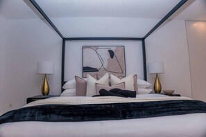 A modern hotel room with a bed, two bedside lamps, a framed abstract artwork, and a black and white color scheme.