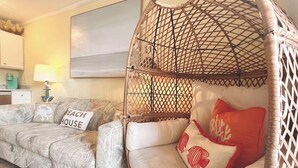 Ein Zimmer mit einem Hängekorbstuhl, einem Sofa mit Kissen mit der Aufschrift 'Beach House' und einer Lampe.