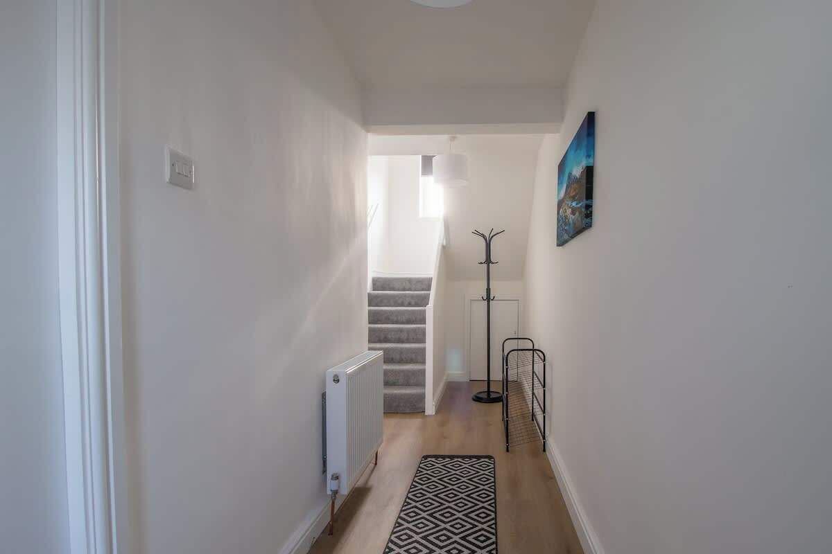 Un pasillo estrecho con un radiador, un tapete estampado, un perchero y una escalera que lleva a otra habitación.