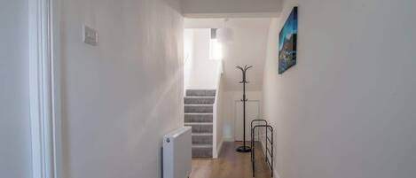 Un pasillo estrecho con un radiador, un tapete estampado, un perchero y una escalera que lleva a otra habitación.