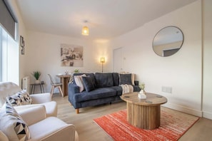 Een moderne woonkamer met een donkerblauwe bank, een ronde salontafel en een rood vloerkleed.
