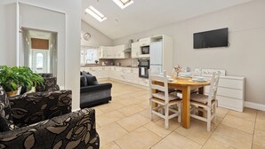 A modern kitchen with white cabinets, a dining table with chairs, and a TV mounted on the wall.