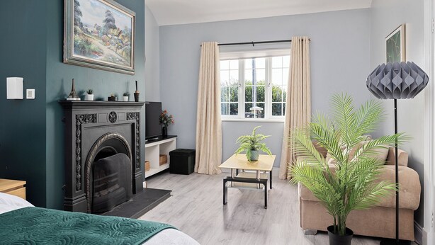 A modern living room with a fireplace, a dining table, a sofa, and a large window with curtains.