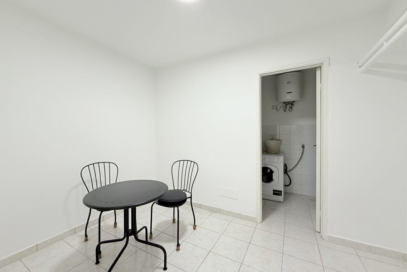 A small, clean room with a table and two chairs, a washing machine, and a door leading to another room.