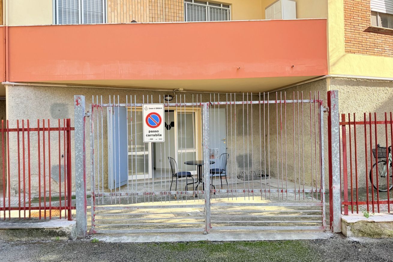 Ingresso recintato a un edificio, con un segnale che indica divieto di parcheggio, una zona coperta con sedie e una bicicletta parcheggiata all'esterno.