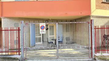Ingresso recintato a un edificio, con un segnale che indica divieto di parcheggio, una zona coperta con sedie e una bicicletta parcheggiata all'esterno.