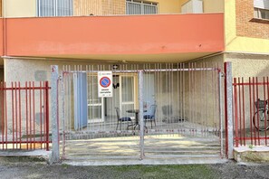 Una entrada protegida a un edificio, con un cartel de no estacionamiento, un área techada con sillas y una bicicleta estacionada afuera.