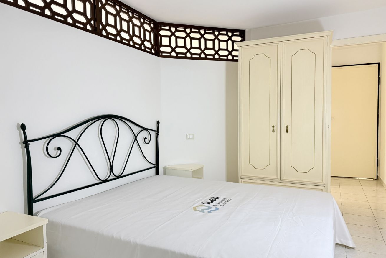 Un dormitorio con cama, armario, mesita de noche y un separador decorativo.