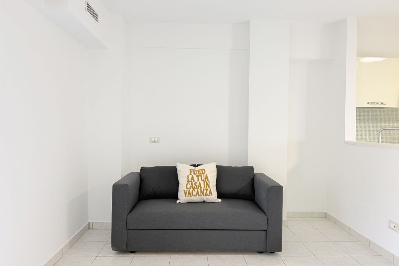 Un sofá gris con un cojín en una habitación con paredes blancas.