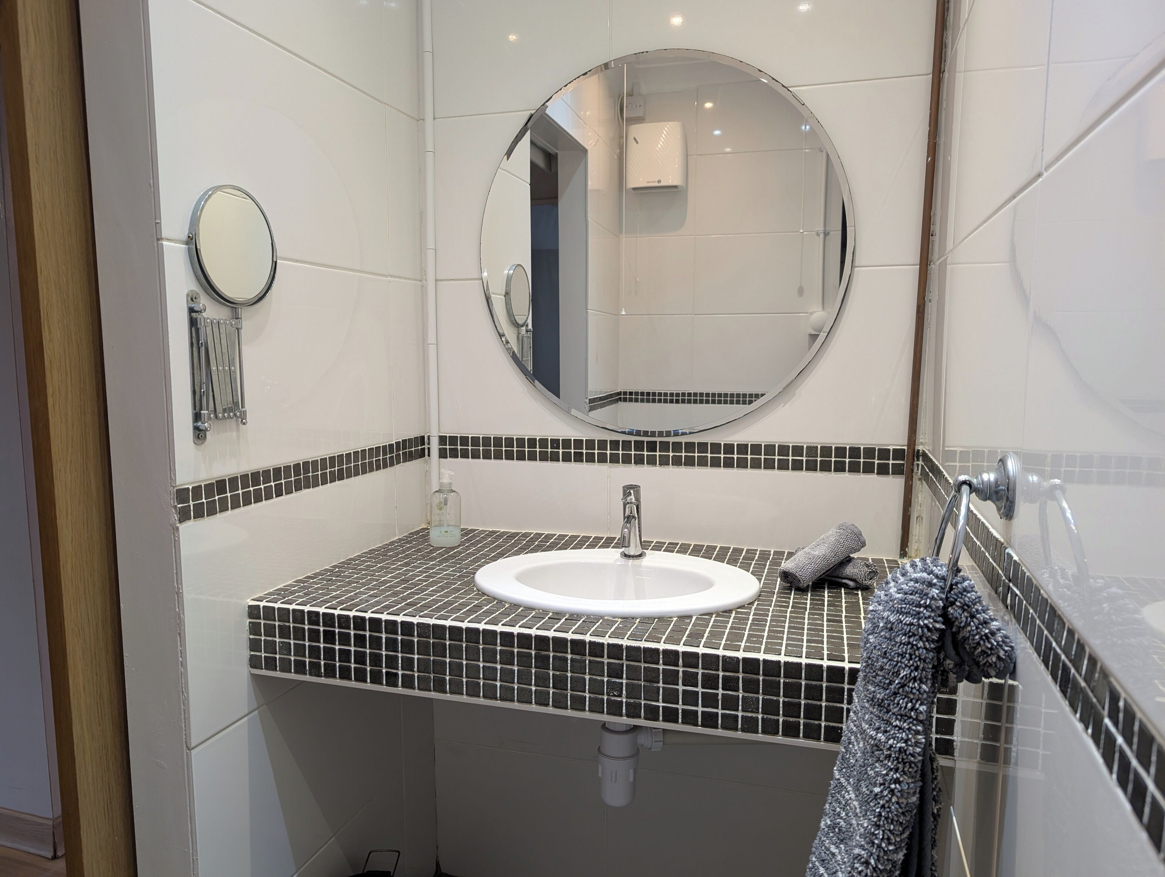 A bathroom with a white sink, a round mirror, and a towel rack.