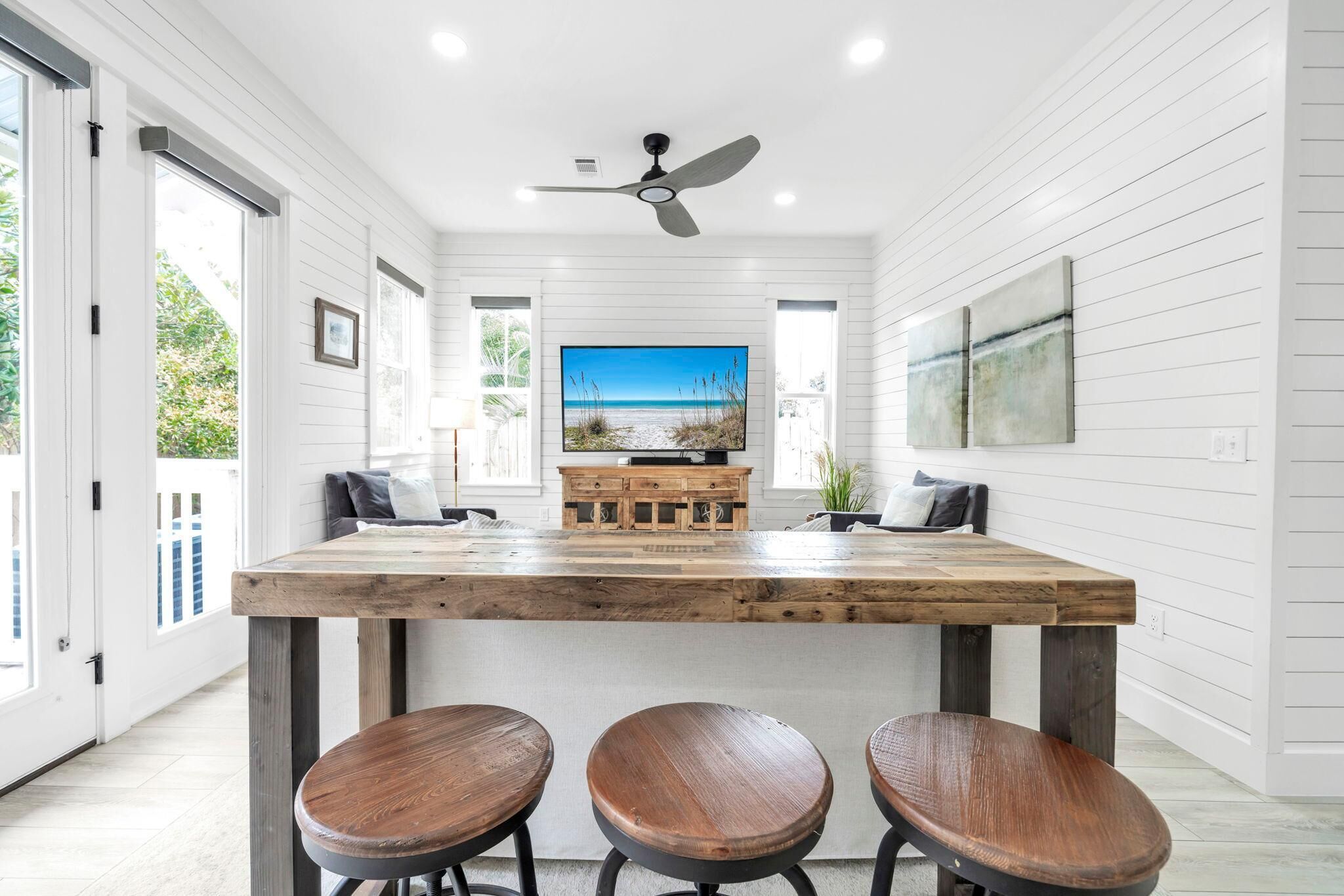 A modern kitchen with a wooden island, bar stools, and a large window with a view of the beach.