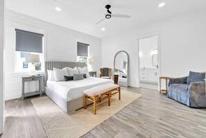 Une chambre à coucher moderne avec un grand lit, des tables de chevet, un banc, un ventilateur de plafond et une vue sur l’extérieur.