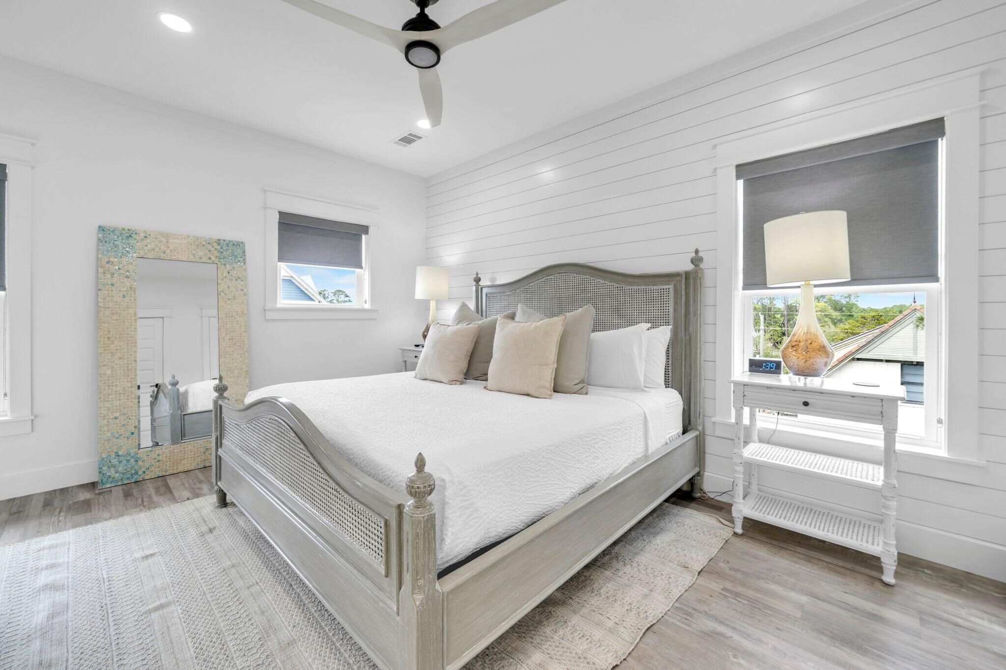A bedroom with a bed, bedside tables, a mirror, and a window with a view.