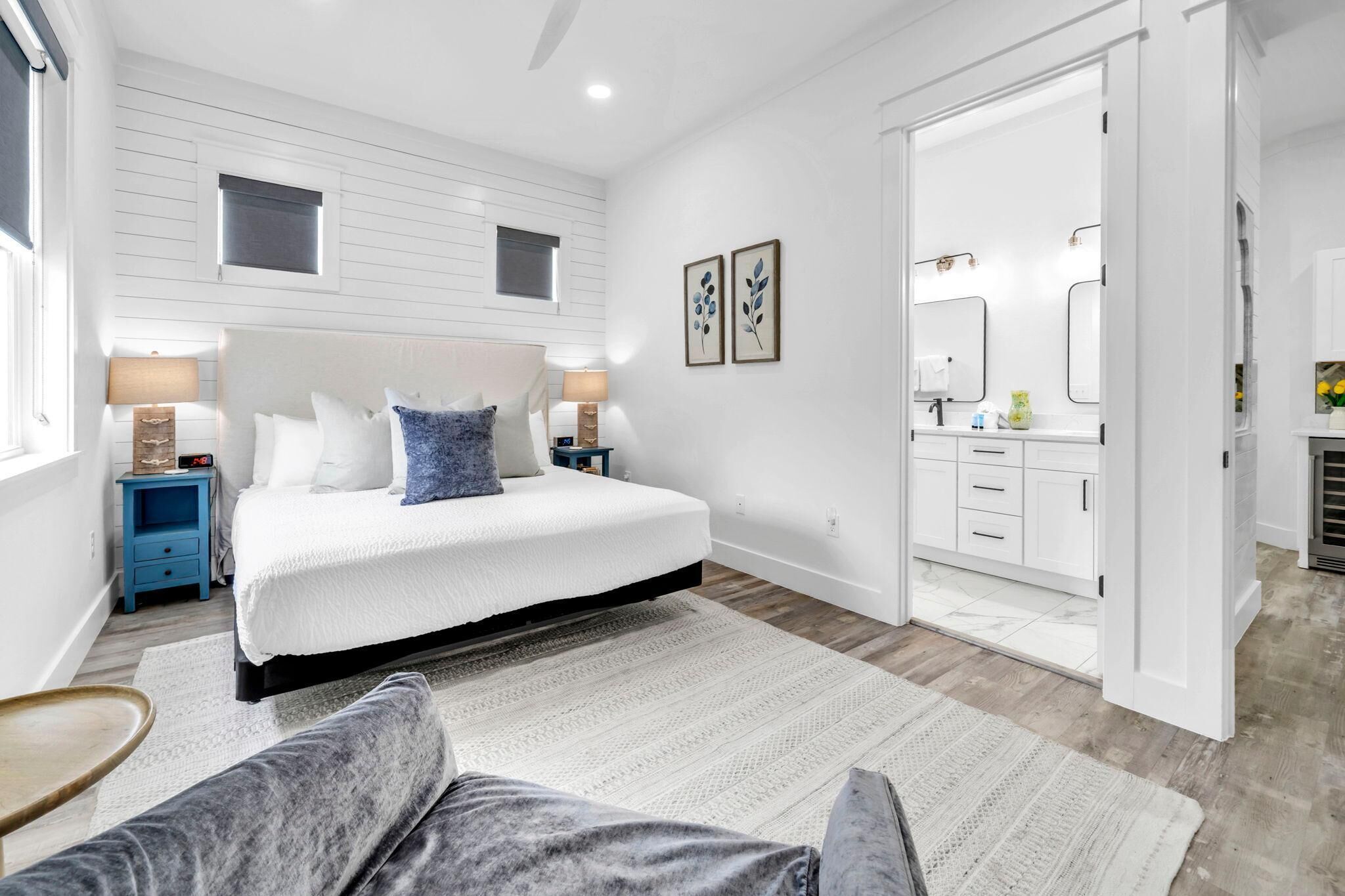 A bedroom with a large bed, bedside tables, a nightstand, a dresser, a mirror, and a door leading to a bathroom.
