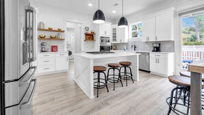 A modern kitchen with white cabinetry, stainless steel appliances, and a central island with stools. - Seapointe Serenity (Santa Rosa Beach)