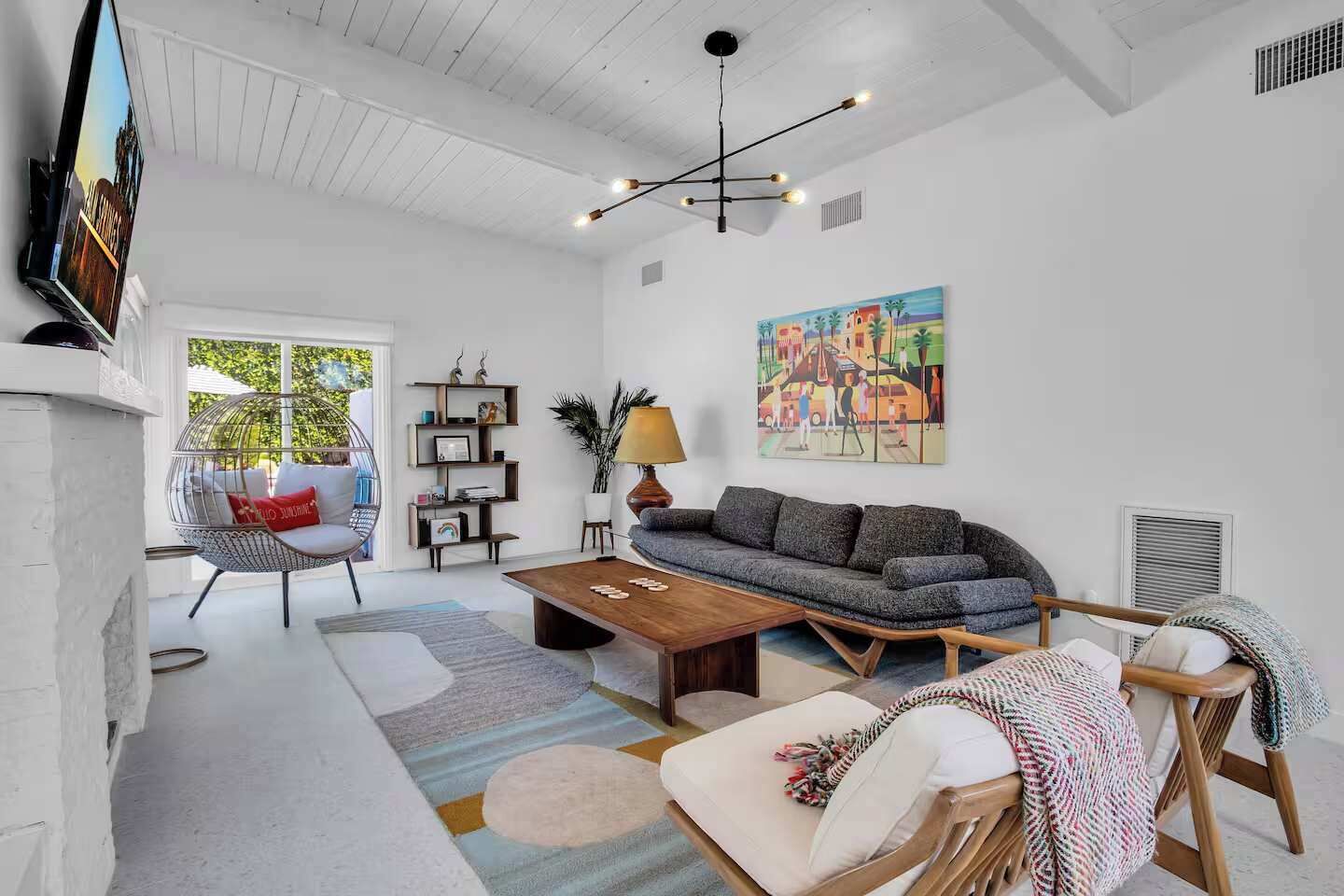 Un salon moderne avec un canapé, une table basse et un fauteuil suspendu. Un tableau orne le mur et un téléviseur y est fixé.