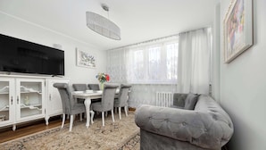 Ein modernes Wohnzimmer mit grauem Sofa, einem Esstisch mit Stühlen, einem Flachbildfernseher und einem dekorativen Teppich.