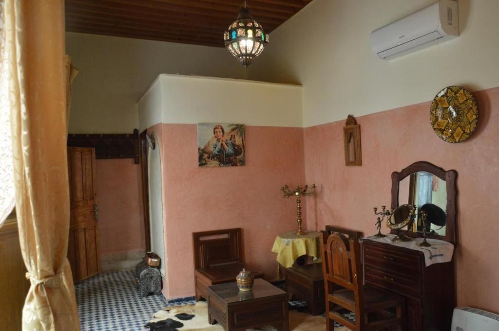 A room with a checkered floor, a wooden cabinet, a table with a vase, a mirror, and a wall clock.