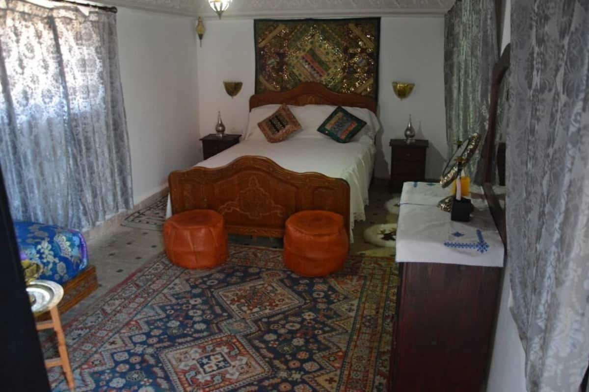 A bedroom with a large bed, two orange ottomans, a patterned rug, and a decorative headboard.