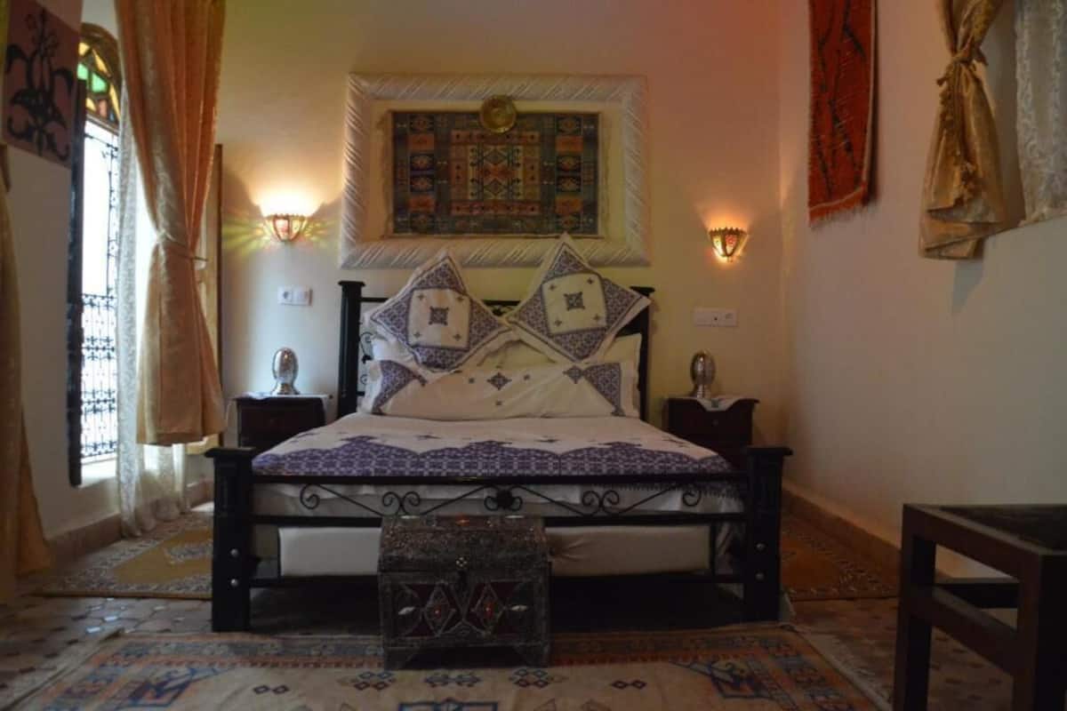 A traditional room with a bed, two wall-mounted lamps, a patterned rug, and a small wooden table.
