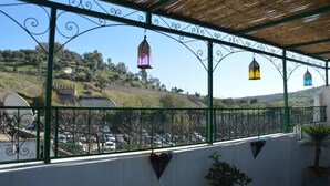 A covered balcony with wrought iron railings, hanging lanterns, and a view of a hilly landscape. - Riad oumkaltoum (Fès)