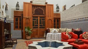 A Moroccan interior with a fountain, red sofas, patterned tiles, and wooden doors. - Riad oumkaltoum (Fès)
