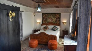 A bedroom with a wooden bed, two wall-mounted lamps, a patterned rug, and a decorative headboard. - Riad oumkaltoum (Fès)