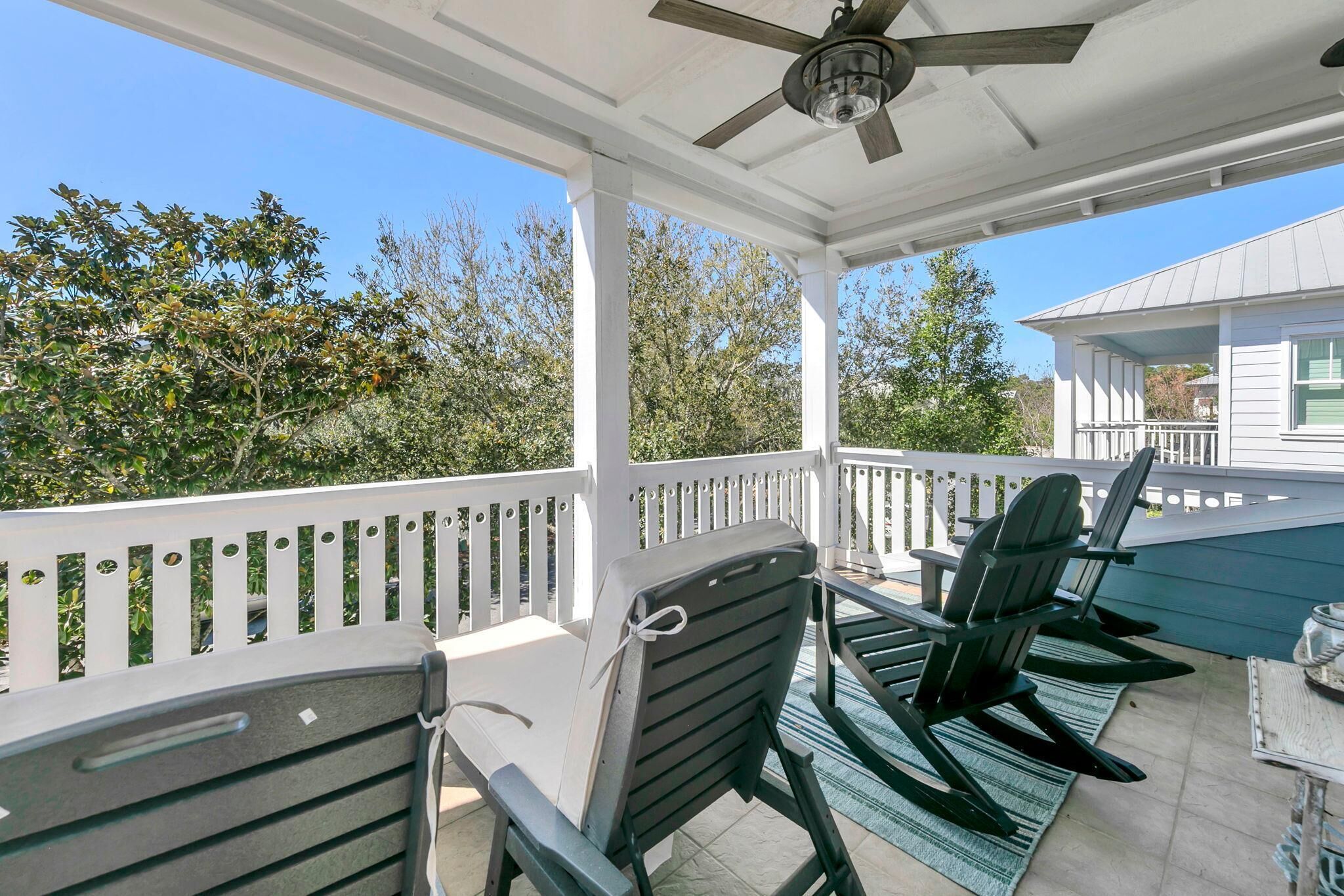 A covered outdoor patio with white railings, black chairs, and a ceiling fan.