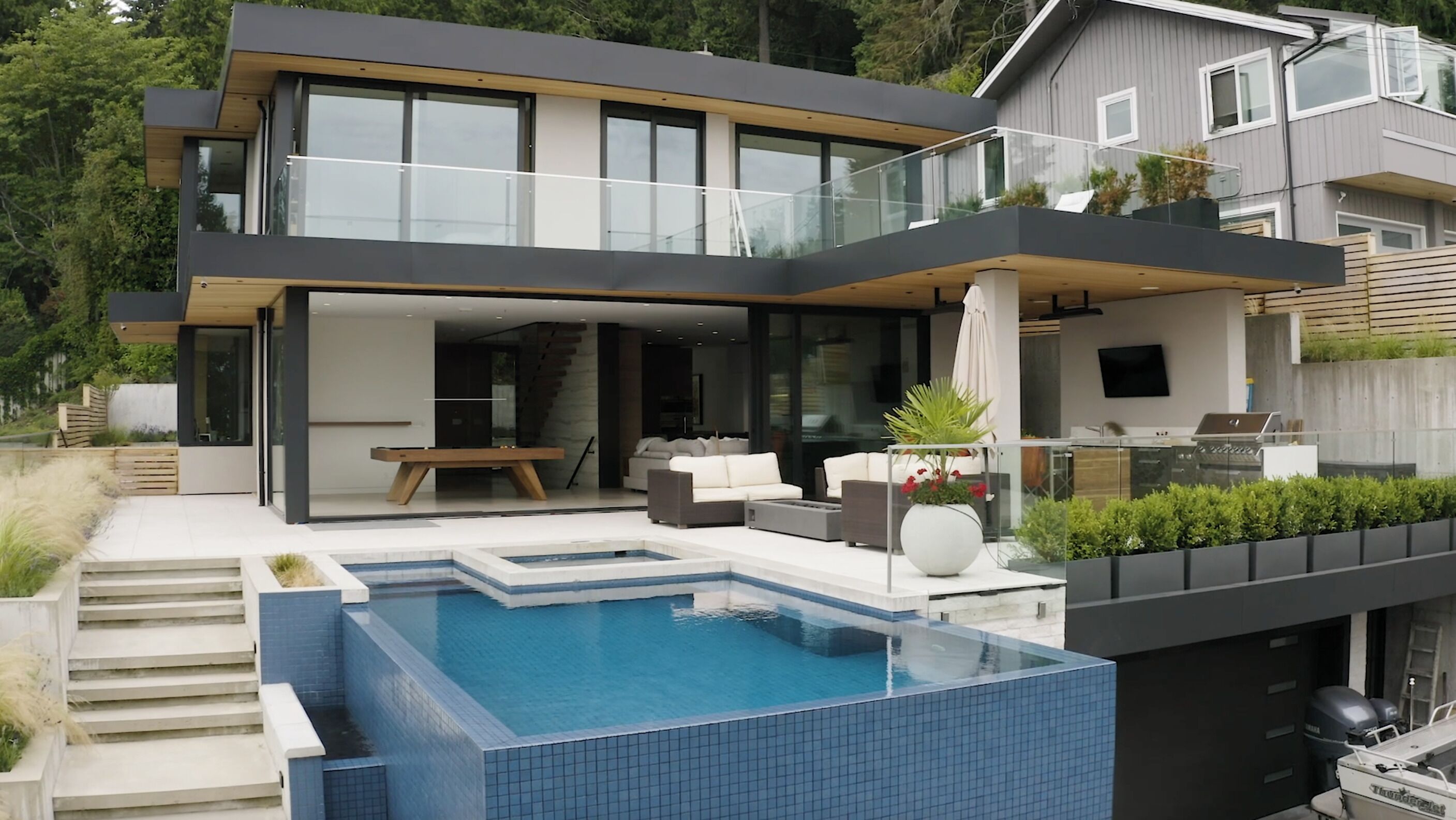 Uma casa moderna de dois andares com piscina, área de estar externa e uma grande varanda de vidro.