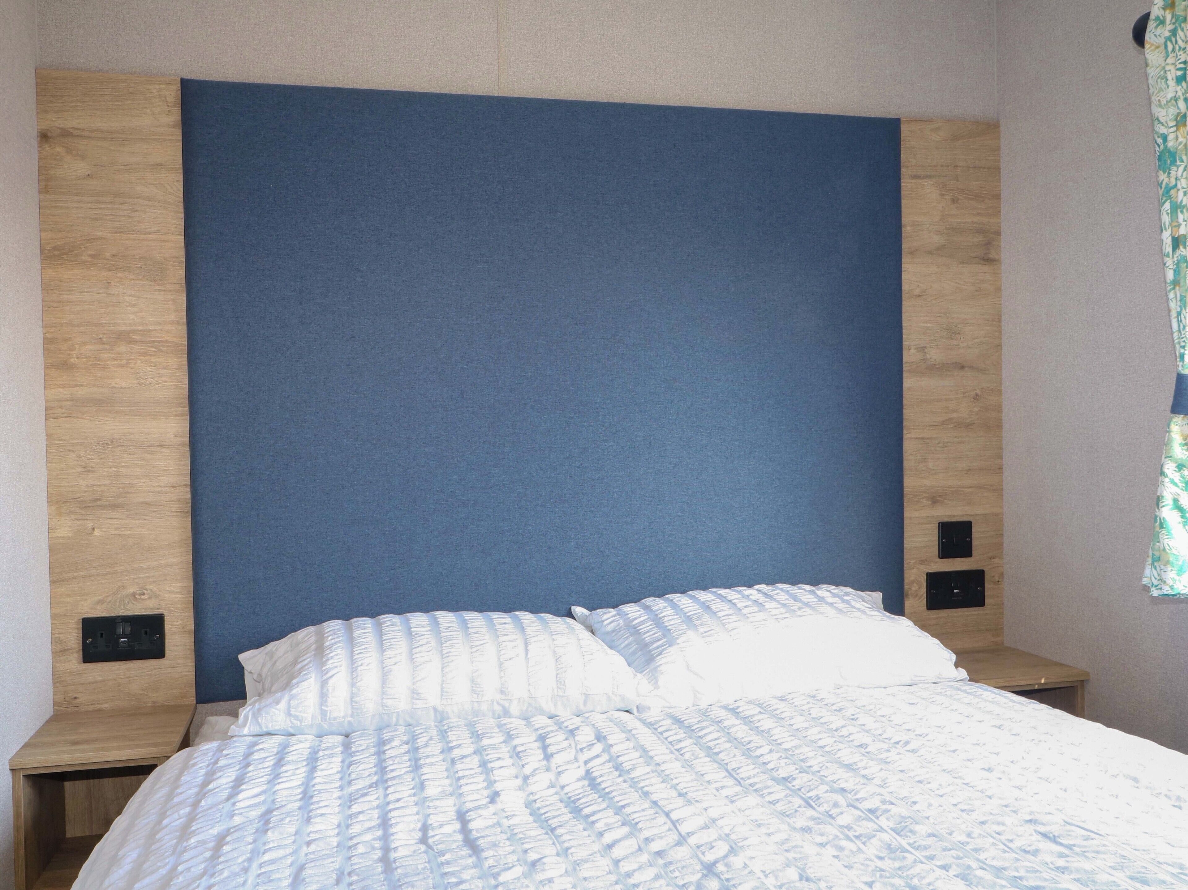 Une chambre à coucher avec un lit, une tête de lit en bois, deux tables de chevet et une prise électrique au mur.